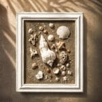 Handcrafted shell canvas with natural seashells on sandy texture in white frame. Perfect coastal decor bringing serene ocean ambiance to your space.